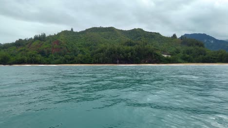 4K-Hawaii-Kauai-Boating-on-ocean-floating-right-to-left-toward-beach-along-green-hillside-to-reveal-waves-crashing-on-rocks