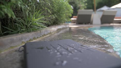 A-black,-basic,-waterproof-laptop-case-with-lines-engraved-in-it-lies-on-the-side-of-a-pool-with-splashes-and-drops-of-water-on-it