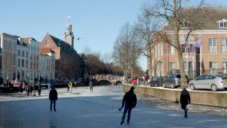 Gente-Patinando-Sobre-Hielo-En-El-Famoso-Canal-Rapenburg-Frente-Al-Edificio-De-La-Academia-En-Leiden,-Países-Bajos-Durante-La-Pandemia