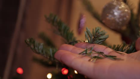 A-male-hand-grabbing-a-fir-leaf-of-a-decorated-Christmas-tree-and-grinding-it-in-his-hand---Close-up
