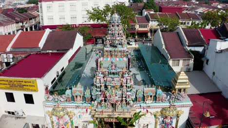 Aerial-approach-of-Sri-Mariamman-Hindu-Temple-with-prayer-flags-and-elaborate-deity-facade,-drone-dolly-in-shot