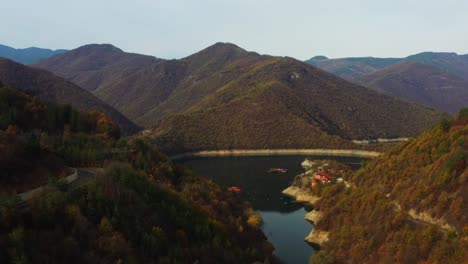 Flying-up-over-Vucha-dam-in-Bulgaria-during-a-colorful-autumn-with-blue-water-in-sight