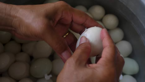 Hand-peeling-hard-boiled-duck-eggs-over-pot-of-water,-close-up
