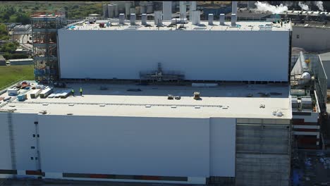 Static-aerial-view-of-construction-workers,-working-at-height-on-a-power-station-roof-top