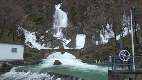 Hillside-gushing-waterfalls-near-dam-after-rain,-Tilt-down