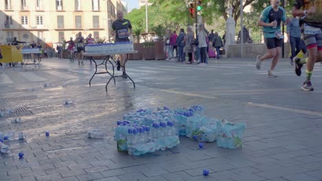 Marathon-runners-running-pass-a-water-checkpoint,-plastic-waste-concept