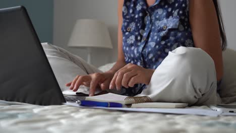 Caucasian-woman-working-from-home-on-bed-typing-on-laptop,-covid-19