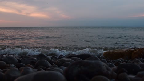 Tiefwinkelaufnahme-Von-Wellen-Des-Ozeans,-Die-Bei-Sonnenuntergang-Gegen-Mehrere-Felsen-Und-Steine-Am-Strand-Krachen