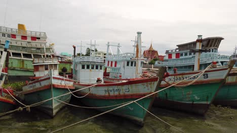 Barcos-De-Pesca-Amarrados-En-El-Barro-En-La-Orilla-De-Un-Río-Durante-La-Marea-Baja-En-Samut-Sakhon,-Tailandia-Y-Esperando-Ser-Desplegados-Nuevamente