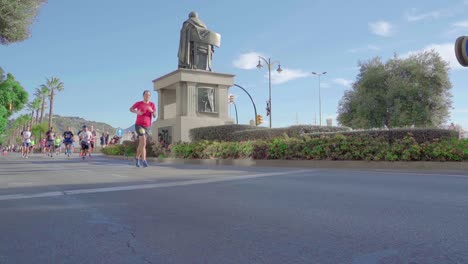 Marathon-runners-run-past-Monumento-Marqués-de-Heredia-in-Malaga,-Spain,-low-angle,-real-time-shot