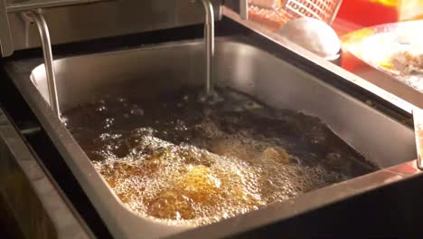 Battered-Fish-Being-Placed-In-Hot-Oil-Deep-Fryer-By-Hand