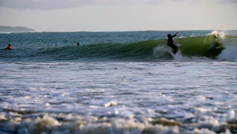 Einheimischer-Surfer-Fängt-Und-Reitet-Vor-Anderen-Surfern-In-Zeitlupe-Eine-Große-Welle,-Linke-Kamerafahrt
