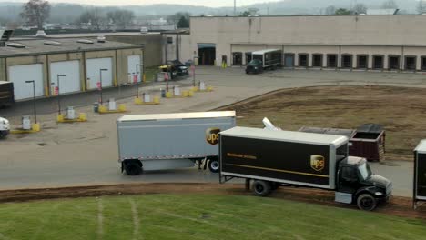 Aerial-tracking-shot-of-UPS-truck-and-trailer-entering-distribution-center