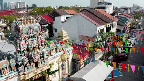 Sri-Mariamman-Hindu-Temple-with-prayer-flags-extending-out-and-blackbird-flies-at-the-end,-Aerial-drone-orbit-around-shot