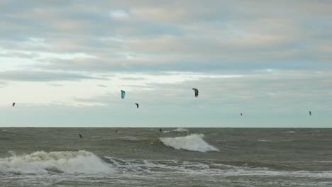 A-group-of-people-engaged-in-kitesurfing-in-sunny-autumn-day,-high-waves,-Baltic-Sea-Karosta-beach-in-Liepaja,-wide-shot