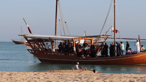 A-view-of-traditional-wooden-boat-known-as-Dhow,-carrying-a-group-of-local-people-singing-and-dancing-at-Katara-Village,-Doha,-Qatar