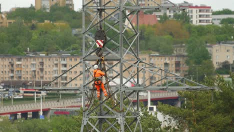The-climber-works-on-a-high-voltage-pole-that-is-being-prepared-to-be-lifted-by-a-crane
