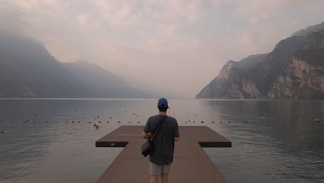 Aerial-View-of-Man-Walking-on-Wooden-Dock-at-Scenic-Lake-Garda,-Northern-Italy
