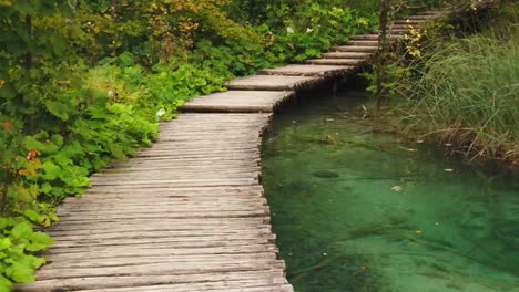 Slow-motion-walk-along-a-wooden-boardwalk-above-a-turquoise-flowing-pool-of-water-in-Plitvice-Lakes-National-Park-in-Croatia,-Europe