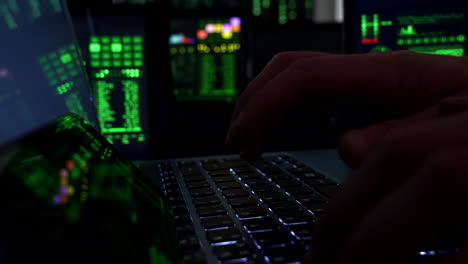 Male-hands-at-keyboard-in-dark-room-with-multiple-screens,-Internet-Fraud
