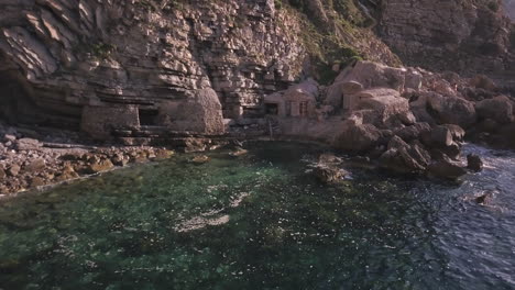 Intriguing-hidden-fisherman's-huts-on-the-rocky-water's-edge-Ibiza,-drone