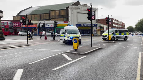 A-police-vehicle-pulls-up-behind-cordon-tape-at-a-junction-and-an-officer-gets-out-at-a-murder-crime-scene-in-East-London