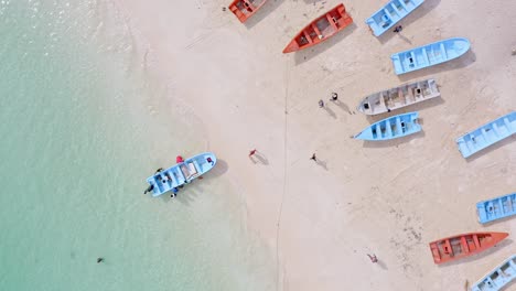Group-tourist-entering-boat-on-sea-shore-for-boat-ride-trip-on-Caribbean-Sea---Drone-top-down-shot