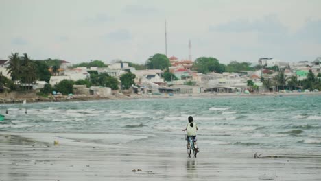 Little-girl-rides-bicycle-on-Vietnamese-seashore-of-Mui-Ne-beach,-near-fisherman-village