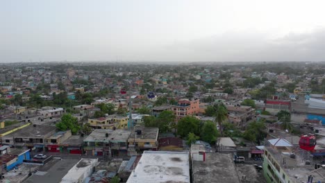 Drohne-Schwebt-über-Schmutzigen-Wohndächern-In-Santo-Domingo,-Während-Rot-weiße-Und-Blaue-Seilbahnen-Aneinander-Vorbeifahren,-Luftaufnahme,-Dominikanische-Republik