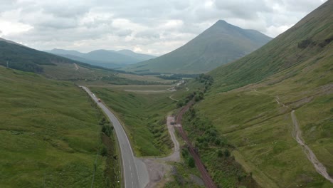 Dolly-forward-drone-shot-of-cars-driving-through-the-scottish-highlands