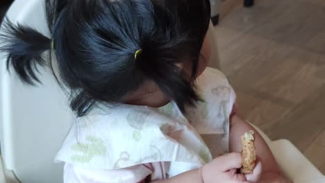 Asiatisches-Süßes-Mädchen,-Das-Ihr-Hausgemachtes-Essen-Auf-Dem-Babyfütterungsstuhl-Isst
