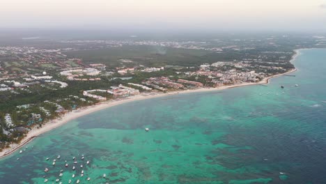 Row-of-resorts-and-boats-at-Punta-Cana-Dominican-Republic-beach,-Aerial-pan-right-reveal-shot