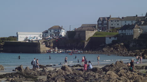 People-Paddling-And-Playing-At-The-Beach-In-The-Lizard-Peninsula-With-Coverack-Harbour-Office-In-Background