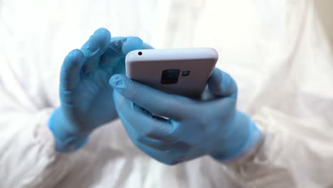 hands-of-doctor-dressed-in-ppe-checking-things-on-mobile-phone-with-finger-and-gloves-on