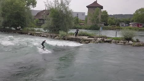 Swiss-surfer-stands-up-on-his-surfboard-on-river-wave-below-weir