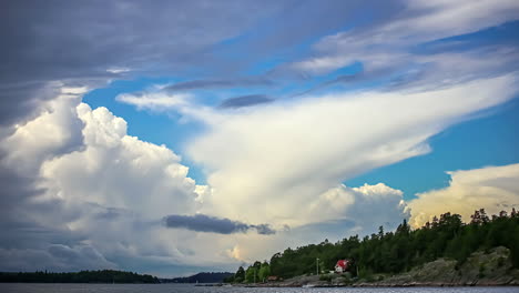 Static-view-of-a-lake-and-white-house-along-with-dense-green-forest-in-summer-rural-landscape-with-white-clouds-passing-by-in-timelapse