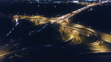 Drones-Aéreos-Vuelan-Sobre-La-Intersección-De-La-Autopista,-Carreteras-Iluminadas,-Automóviles,-Motocicletas,-Autobuses-Y-Camiones-Por-La-Noche-En-La-Moderna-Ciudad-Metropolitana-De-Varsovia,-Polonia