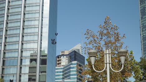 Un-Grupo-De-Limpiadores-De-Ventanas-Colgando-De-Un-Rascacielos-Moderno-En-Una-Zona-Lujosa-Durante-El-Día,-Santiago,-Chile