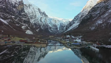 Aerial-slowly-approaching-historic-Gudvangen-above-Unesco-listen-Naeroyfjord---Beautiful-winter-morning-with-sunrise-in-mountain-background-and-reflections-in-crispy-clear-water-surface