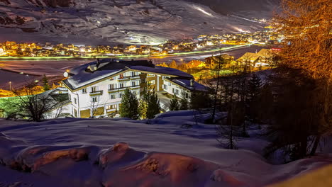 Time-lapse-shot-of-snowy-alps-mountains-in-valley-with-lighting-village-during-evening---Driving-snowcats-on-piste