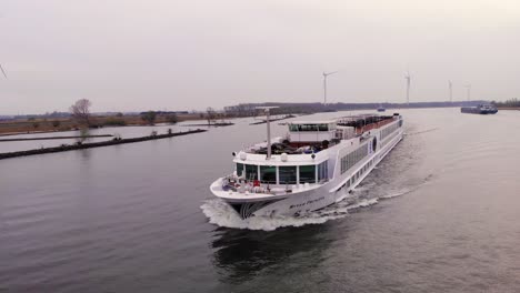Aerial-View-Of-River-Cruise-Ship-Navigating-Along-Oude-Maas-Going-Past-Still-Wind-Turbines-In-Barendrecht