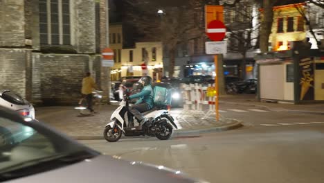 Deliveroo-food-delivery-rider-on-a-scooter-in-the-evening-in-Ghent,-Belgium