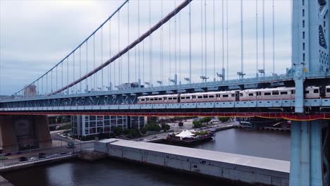 Drone-shot-of-a-subway-train-crossing-the-Ben-Franklin-Bridge-in-Philadelphia,-Pennsylvania