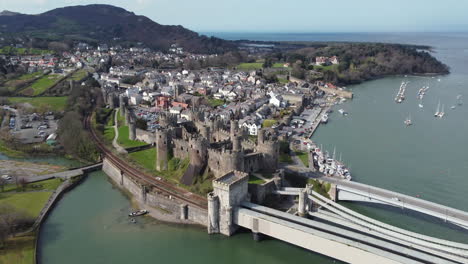 An-aerial-view-of-Conwy-Castle-on-a-sunny-day,-flying-towards-the-castle-with-the-town-in-the-background,-North-Wales,-UK