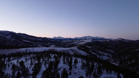 Flug-über-Kiefern-Im-Winter-In-Richtung-Der-Felsigen-Berge-Während-Der-Blauen-Stunde,-Luftaufnahmen