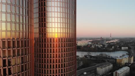 Wunderschöne-Drohnenansicht-Des-Klaren-Rosafarbenen-Himmels-Und-Der-Stadtlandschaft-Von-Riga,-Lettland-Bei-Einem-Goldenen-Sonnenuntergang-Mit-Zwei-Wolkenkratzern-Der-Zunda-Türme-Im-Vordergrund,-Die-Die-Sonne-Reflektieren