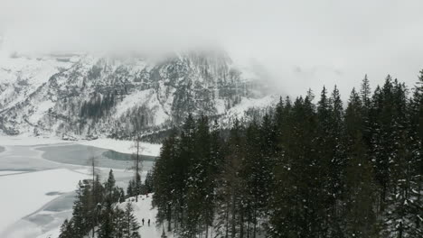 Flug-über-Baumkronen-Mit-Einer-Schneebedeckten-Landschaft-Und-Einem-Zugefrorenen-See-Im-Hintergrund