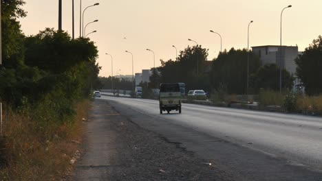 Blick-Vom-Standstreifen-Auf-Den-Vorbeifahrenden-Verkehr-In-Karatschi-Mit-Orangefarbenem-Sonnenuntergangshimmel