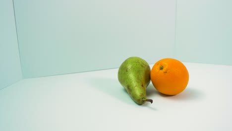 Frische-Große-Grüne-Birne,-Saftige-Orange-Dreht-Sich-Langsam-Auf-Hellblauem-Hintergrund,-Gesundes-Ernährungskonzept,-Nahaufnahme,-Kamera-Nach-Links-Drehend