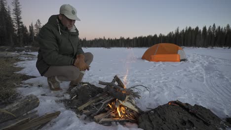 Man-feeding-a-fire-in-the-snow-next-to-his-tent